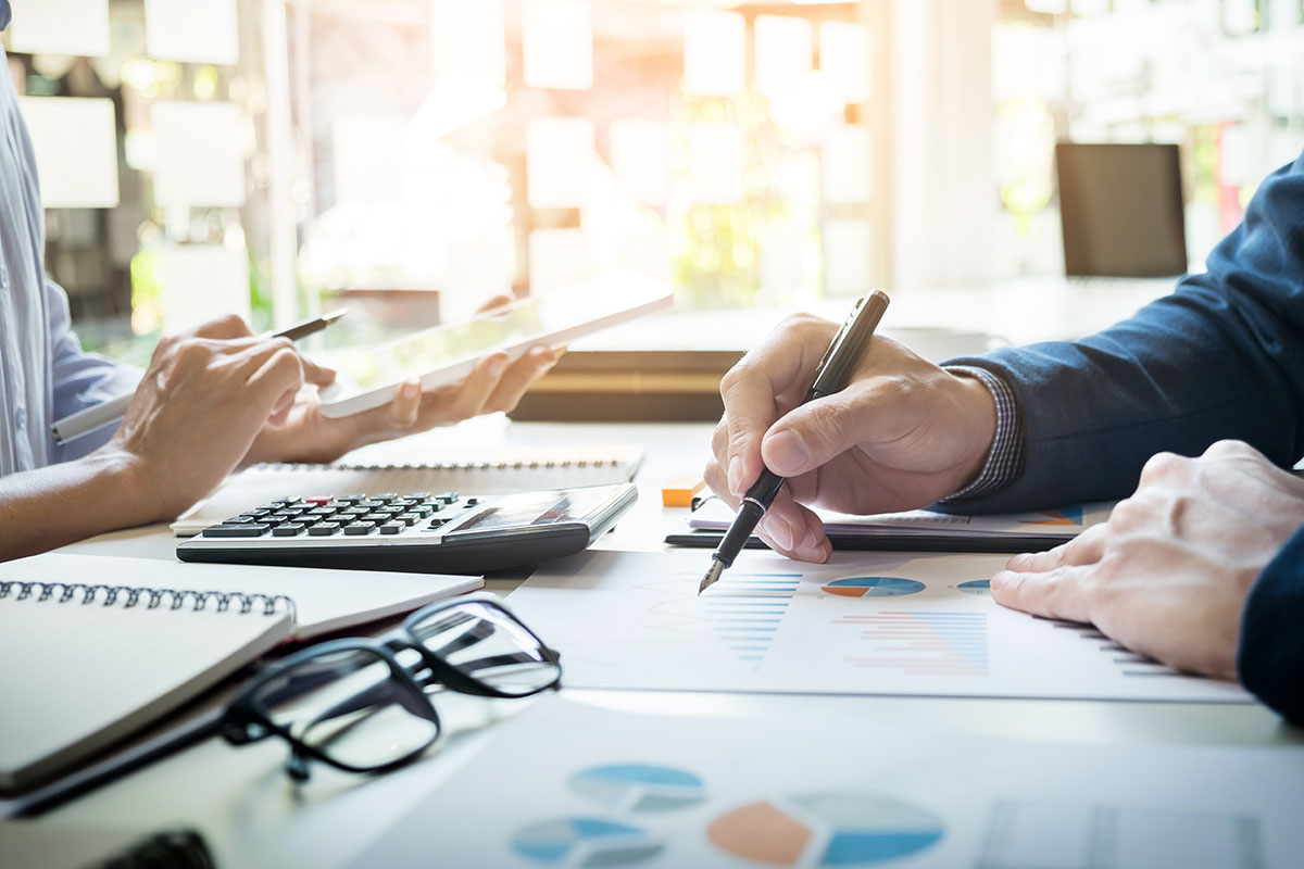 Two pairs of hands holding pens, leaning on a table with charts and office supplies