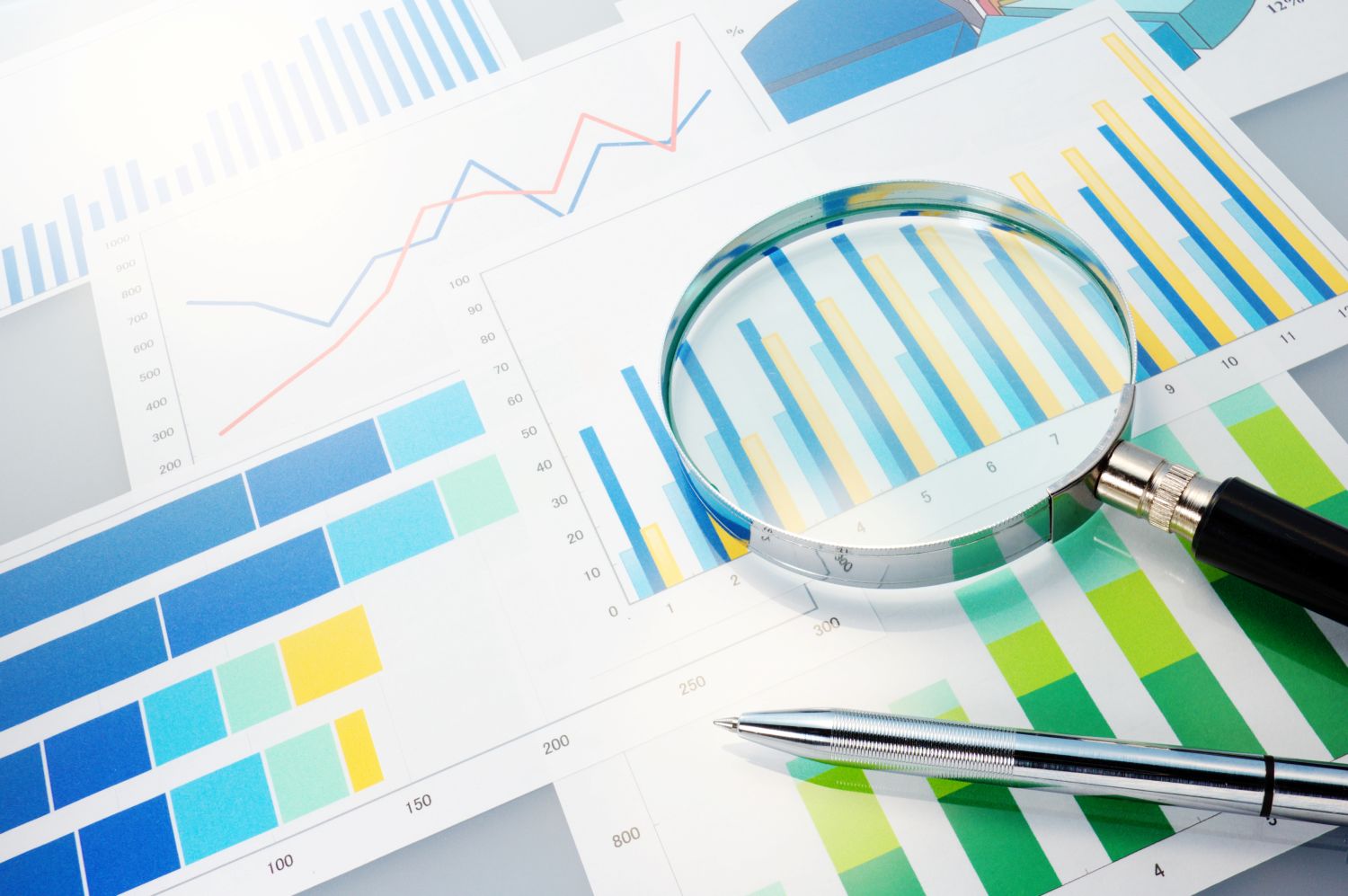 Magnifying glass and pen lying on paper graphs image